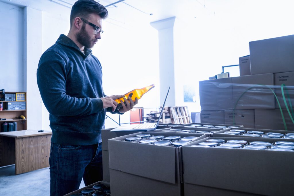 Young man in warehouse quality checking label on beer bottle